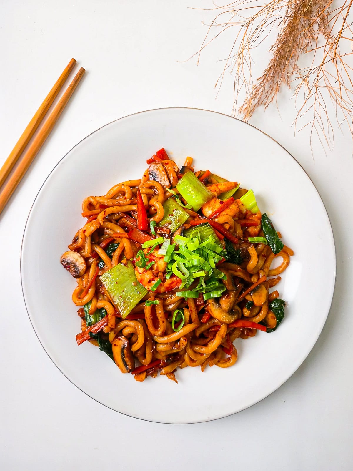 Overhead photo of thick udon noodles stir-fried with shrimp, bok choy, mushrooms, and colorful vegetables topped with fresh green onions.