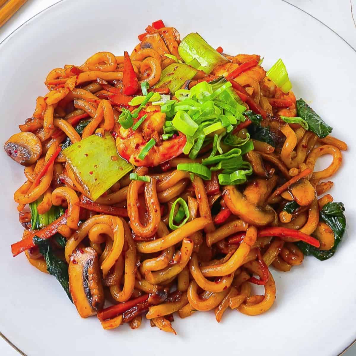 Close-up of shrimp yaki udon stir-fry with bok choy, mushrooms, carrots, and green onions on a white plate.