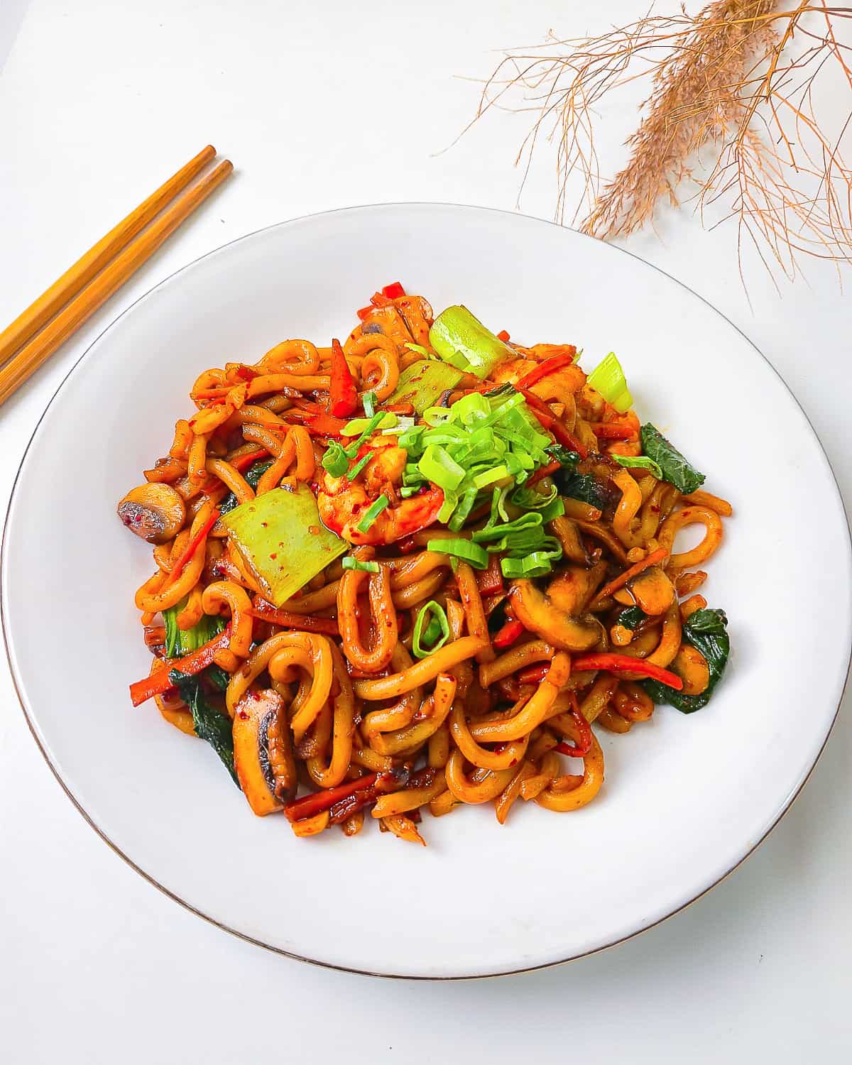 Angled close-up of shrimp yaki udon on a white plate showing thick noodles, bright vegetables, and fresh green onion garnish.