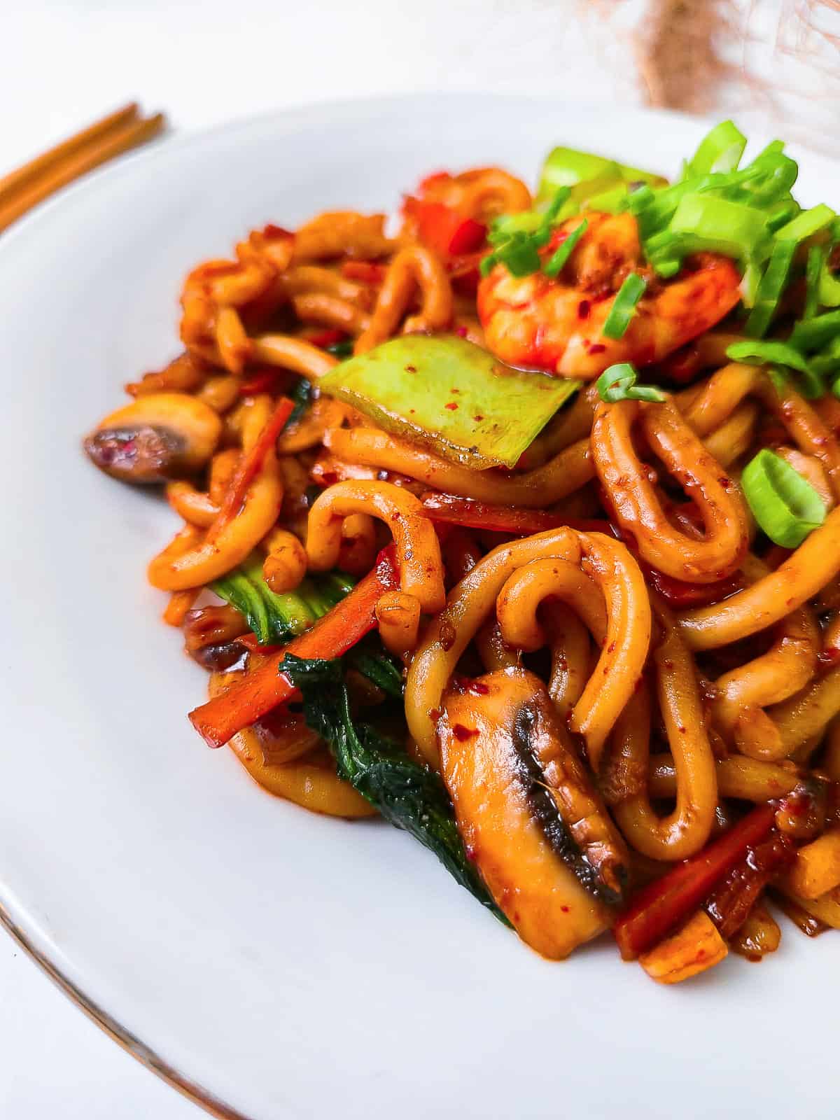 Close-up view of shrimp yaki udon on a white plate showing thick noodles, bright vegetables, and fresh green onion garnish.