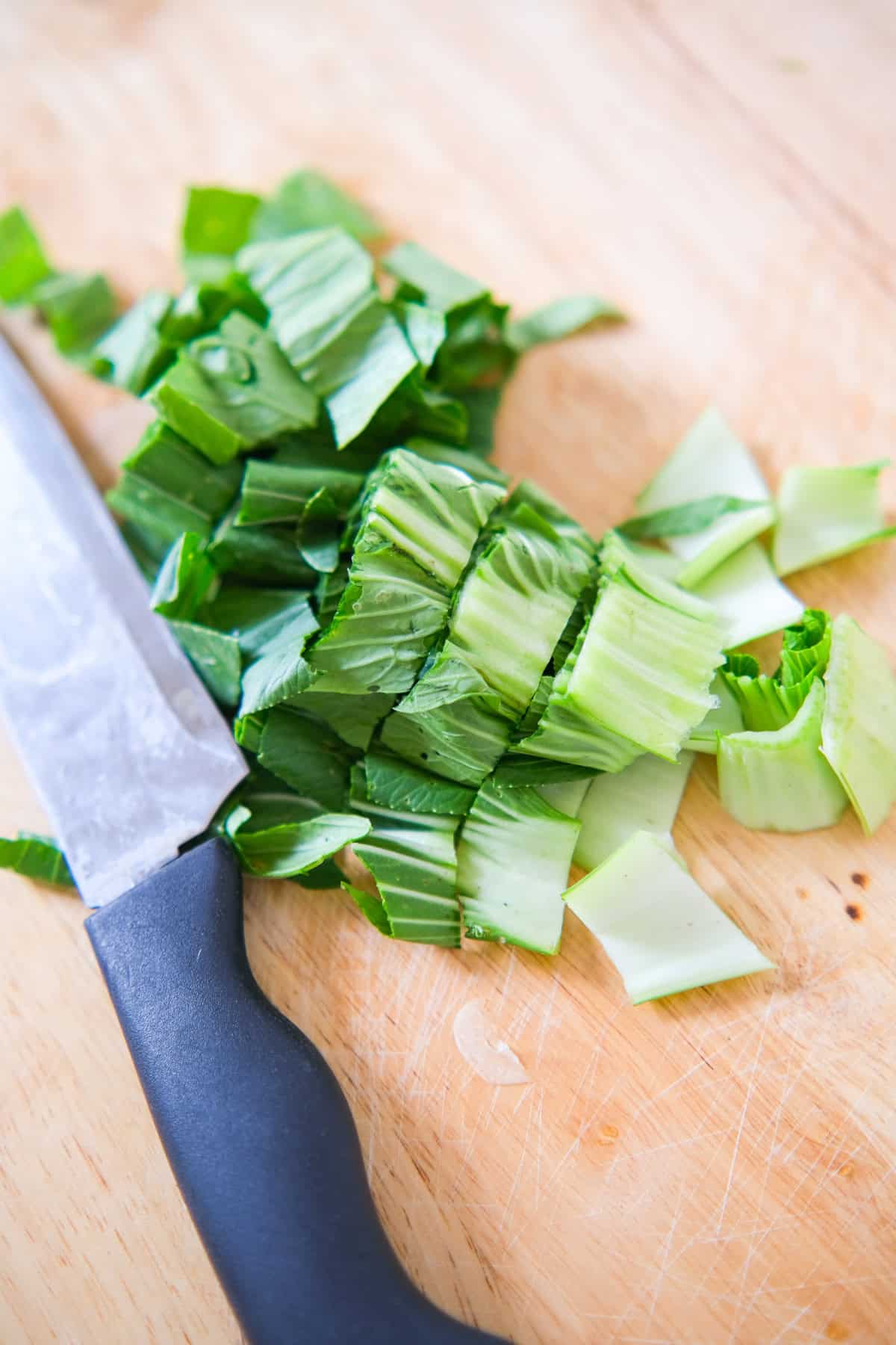 Chopped bok choy on a wooden cutting board next to a knife.