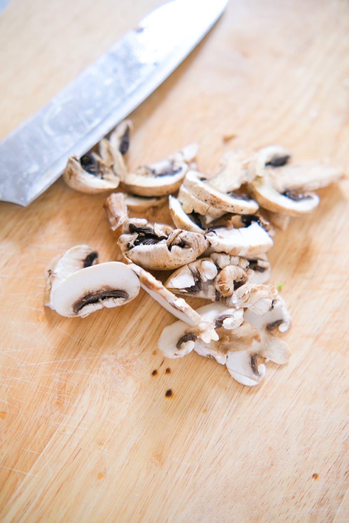 Freshly sliced mushrooms on a wooden cutting board beside a knife.