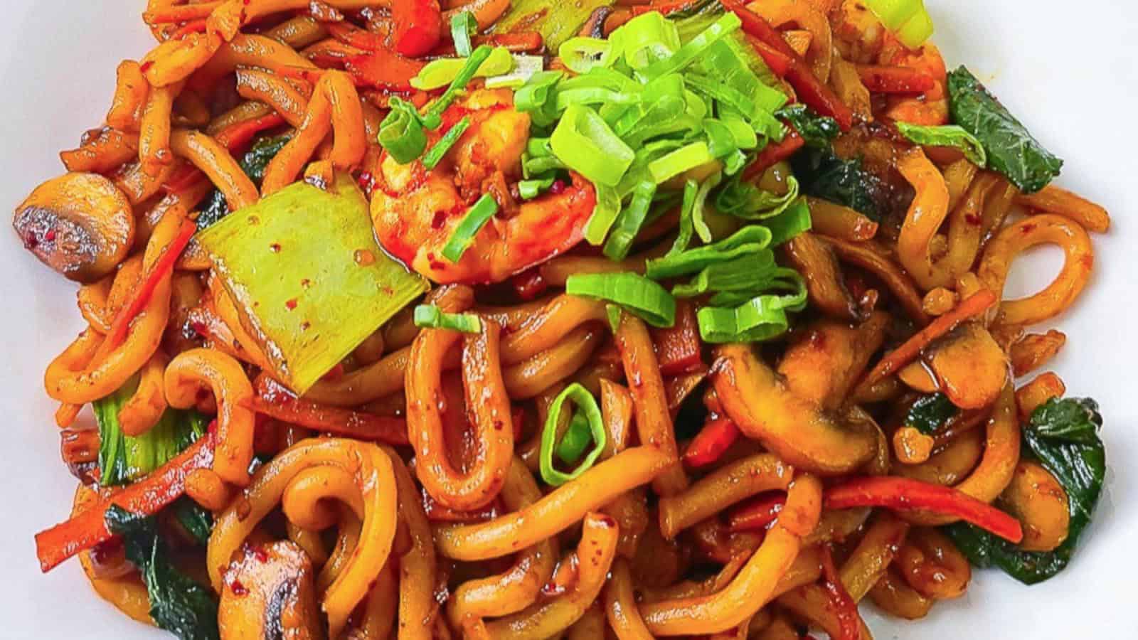 Shrimp yaki udon stir-fry with bok choy, mushrooms, carrots, and green onions on a white plate.