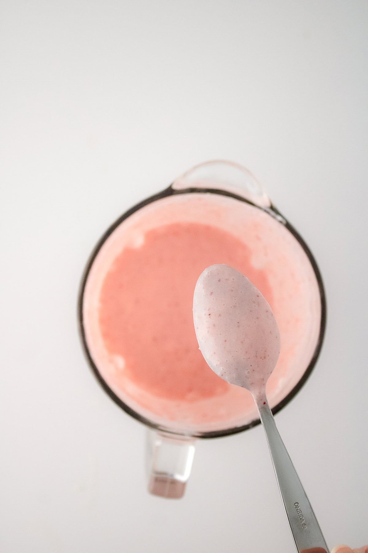 Smooth blended strawberry mixture in a blender with a spoonful of creamy pink mix.