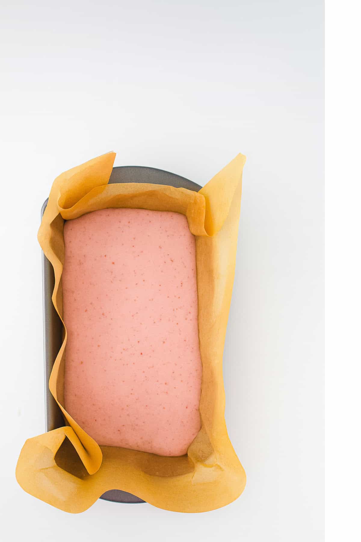 Freshly poured strawberry ice cream base in parchment-lined loaf pan.