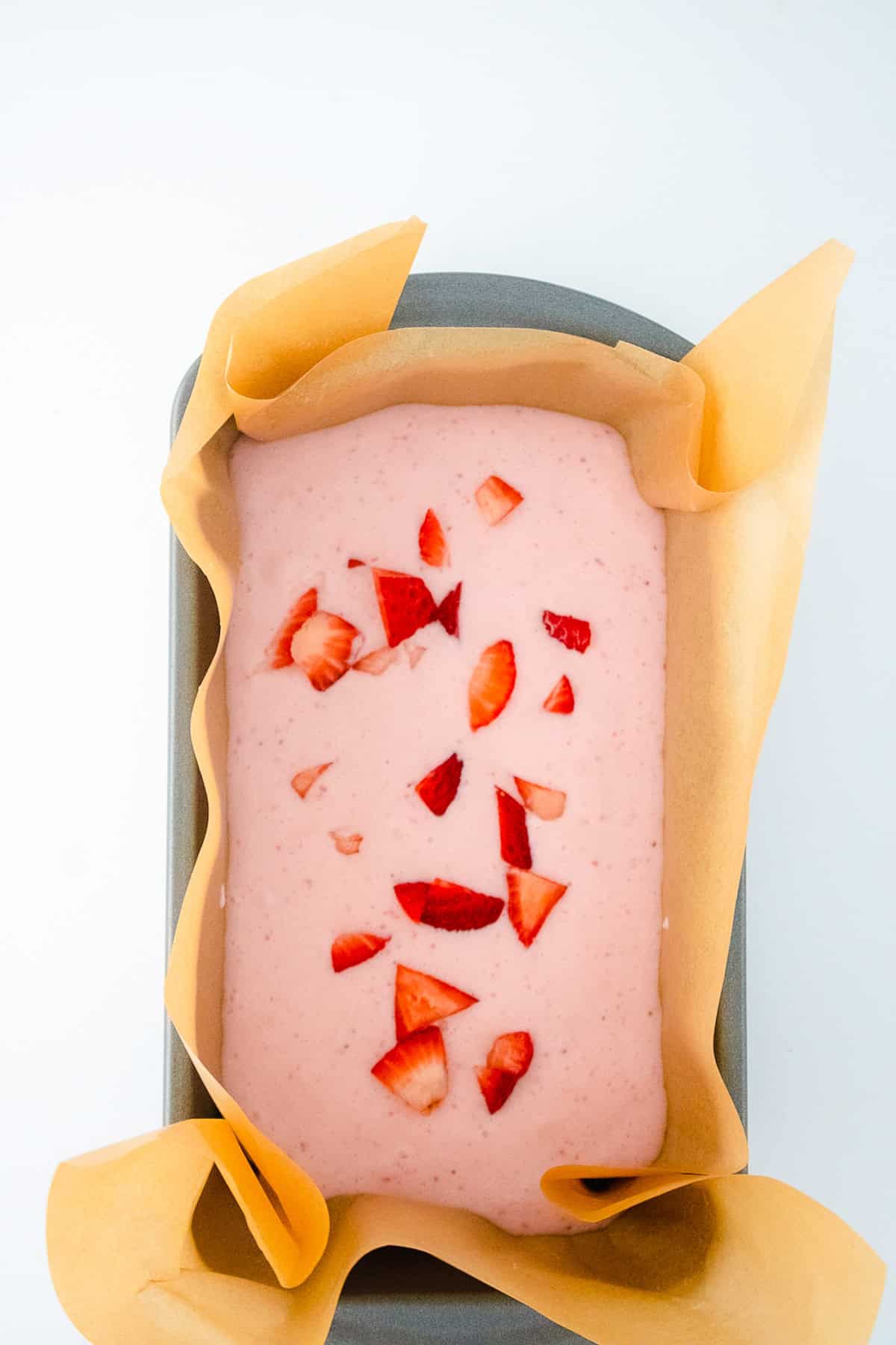 Strawberry ice cream mixture topped with chopped strawberries before freezing.