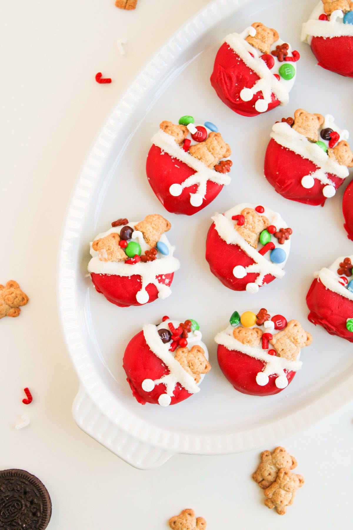 A neat tray of red and white dipped Oreo cookies decorated with holiday candy pieces and teddy bear crackers.