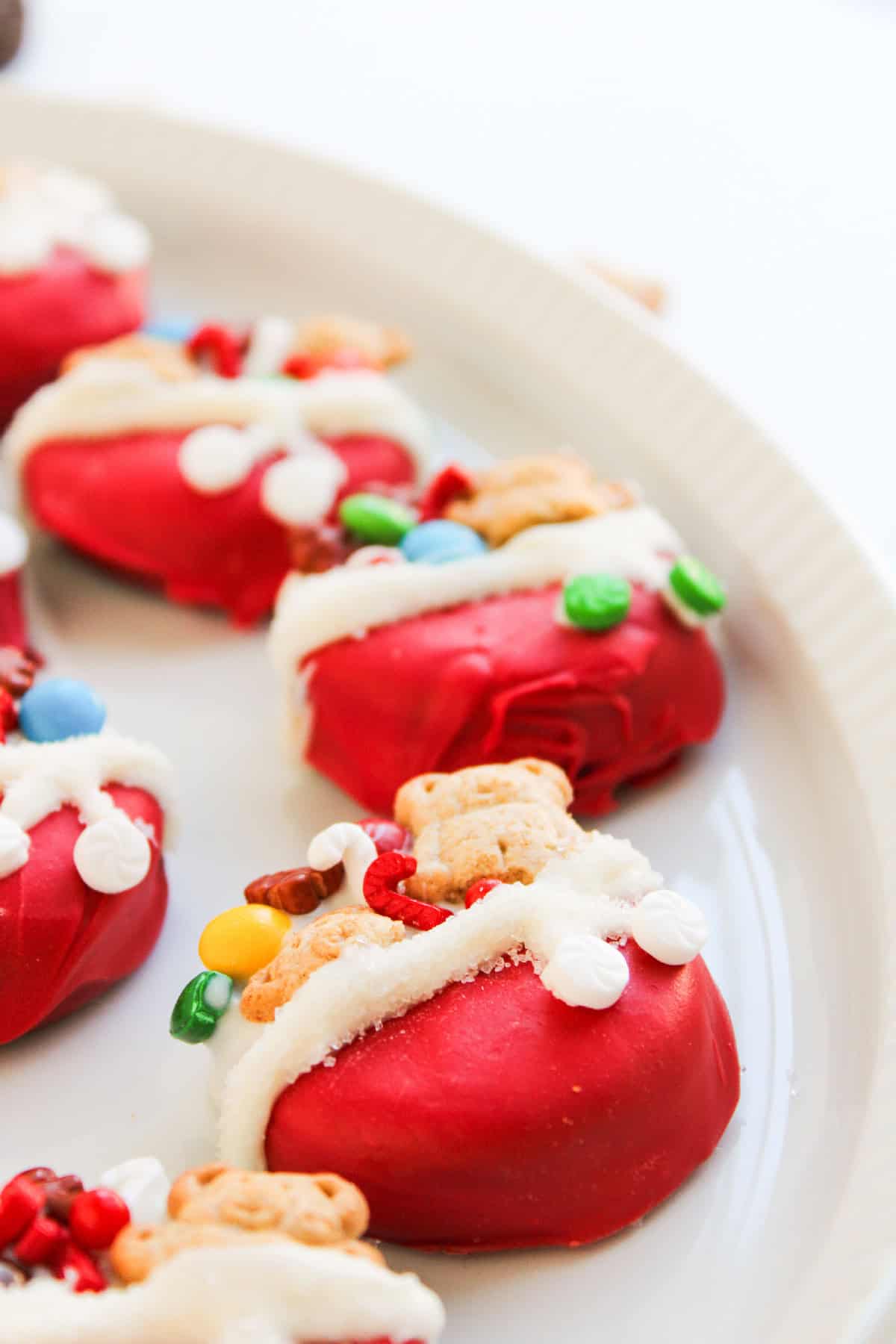 Low-angle view of Christmas Oreo cookies topped with mini candies and teddy grahams on a white serving dish.