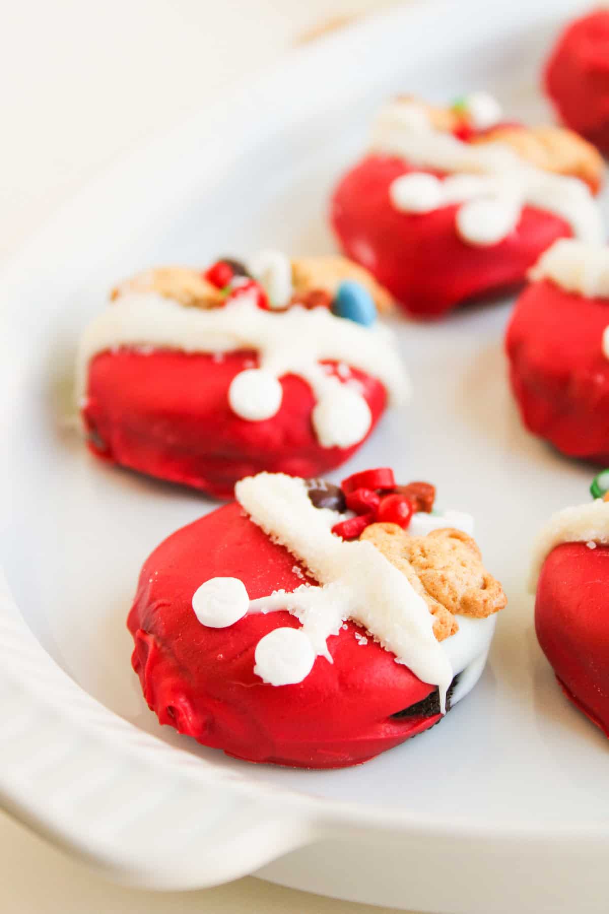 Side angle of Christmas Oreo cookies on a white platter, showing details of candy toppings and white frosting trim.