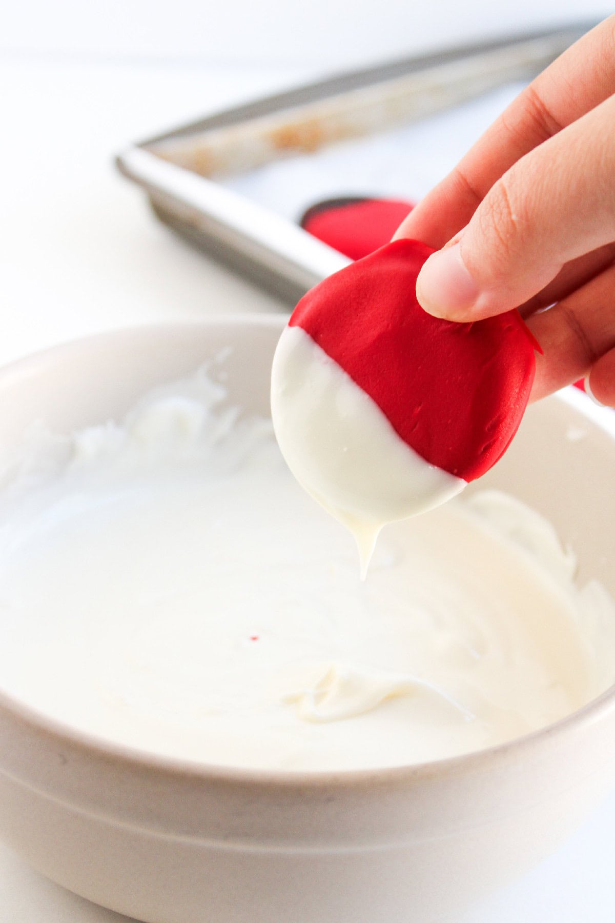 A hand dipping the red-coated cookie into melted white chocolate to create a layered effect.