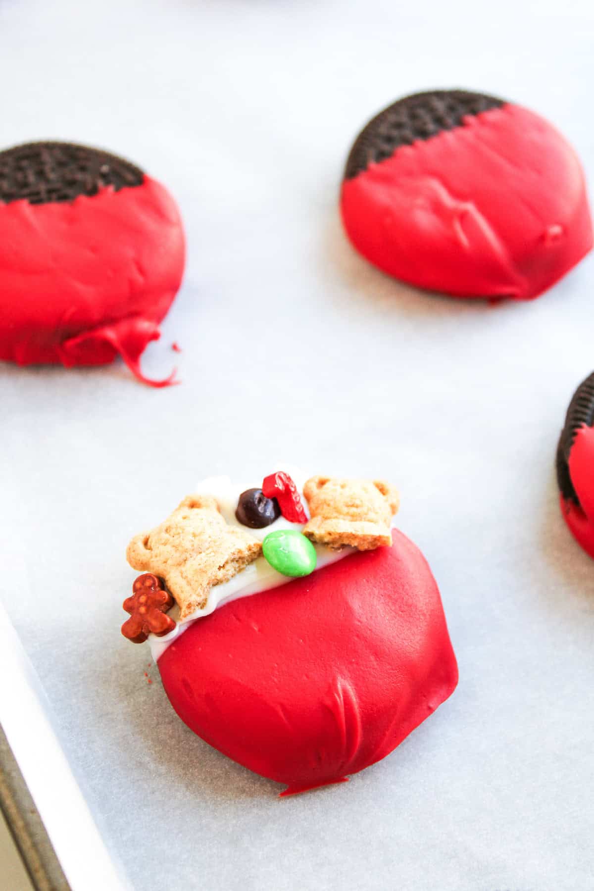 A red and white dipped cookie topped with mini teddy bear crackers, candy pieces, and festive decorations.
