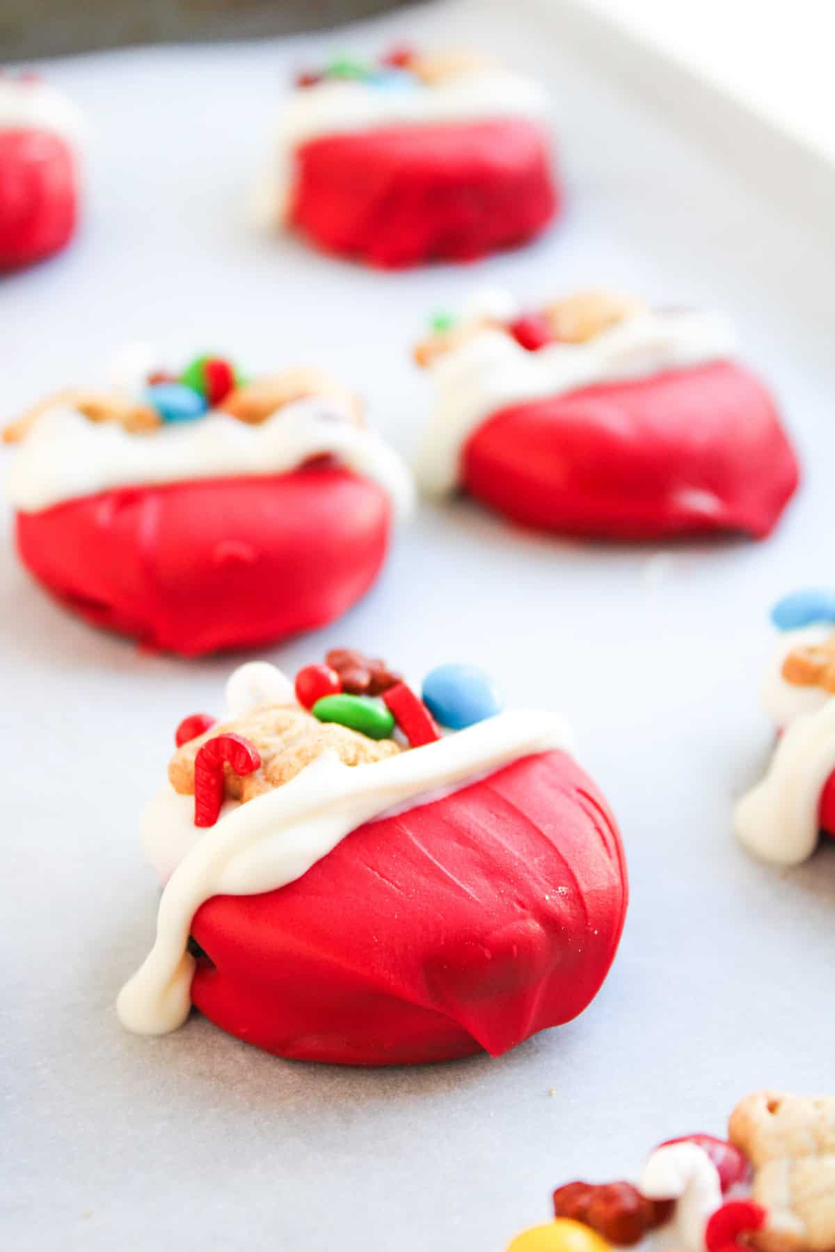 A close-up view of a red and white dipped cookie decorated with holiday candies and teddy bear crackers.