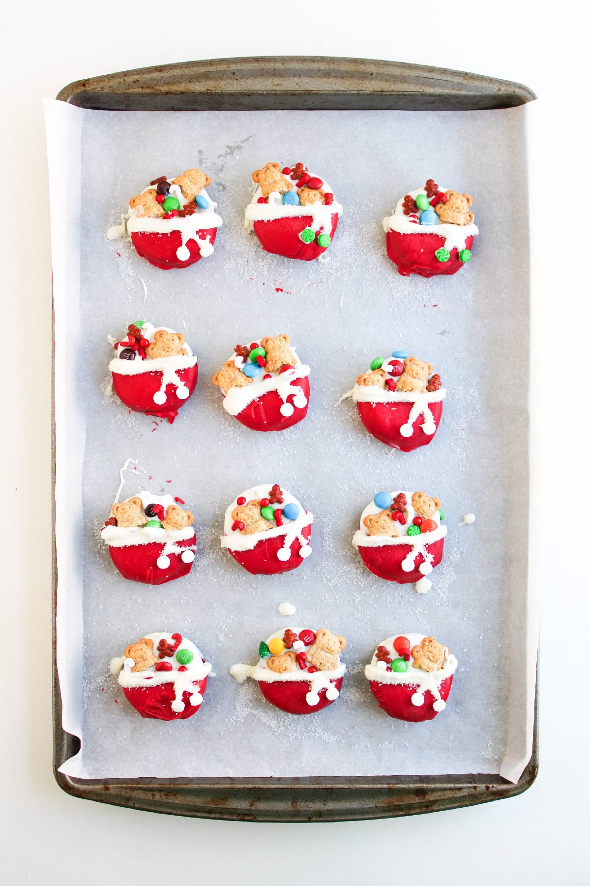 A tray of finished Christmas Oreo cookies decorated with red and white chocolate and festive toppings.
