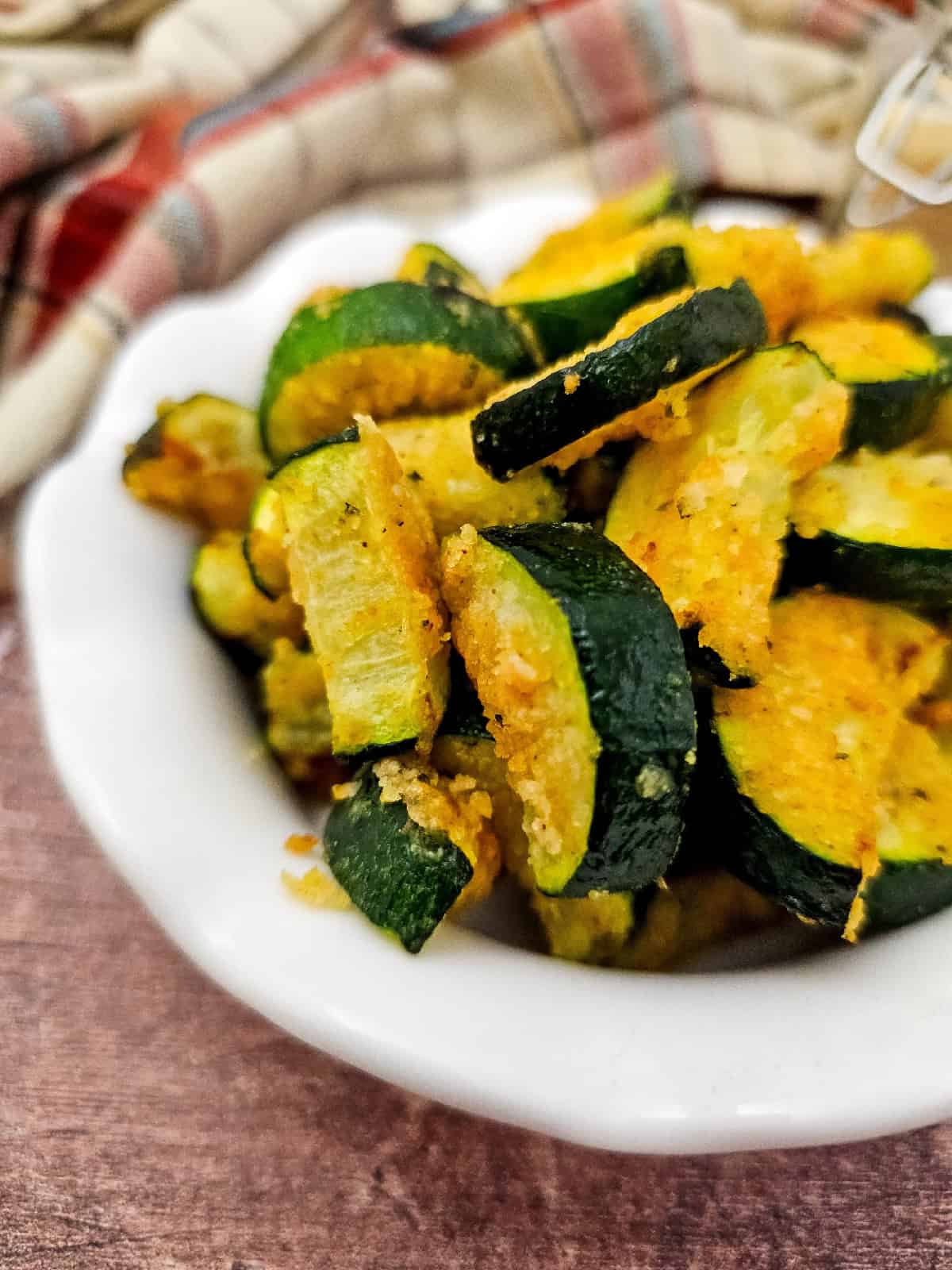 Angled close-up of air fryer zucchini parmesan with crispy coating, showing the texture of the breading and vibrant green zucchini skin.