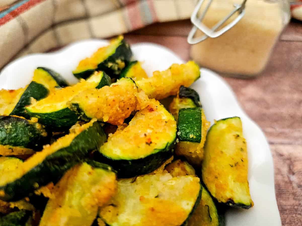 Macro shot of crispy air fryer zucchini parmesan pieces in a white bowl, highlighting the golden coating and tender green zucchini slices.