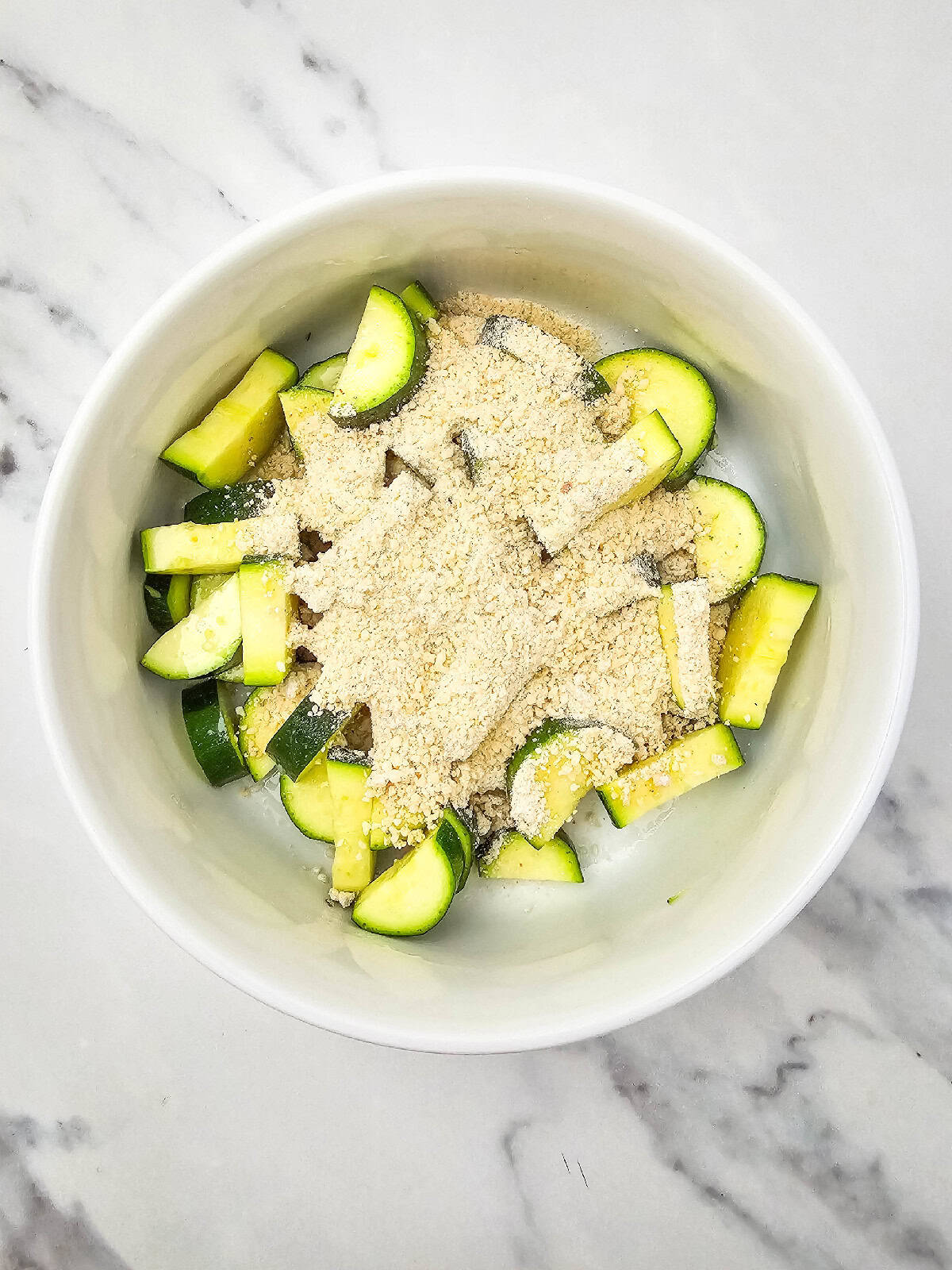 Breadcrumb and vegan parmesan mixture fully combined in a white mixing bowl on a marble countertop.