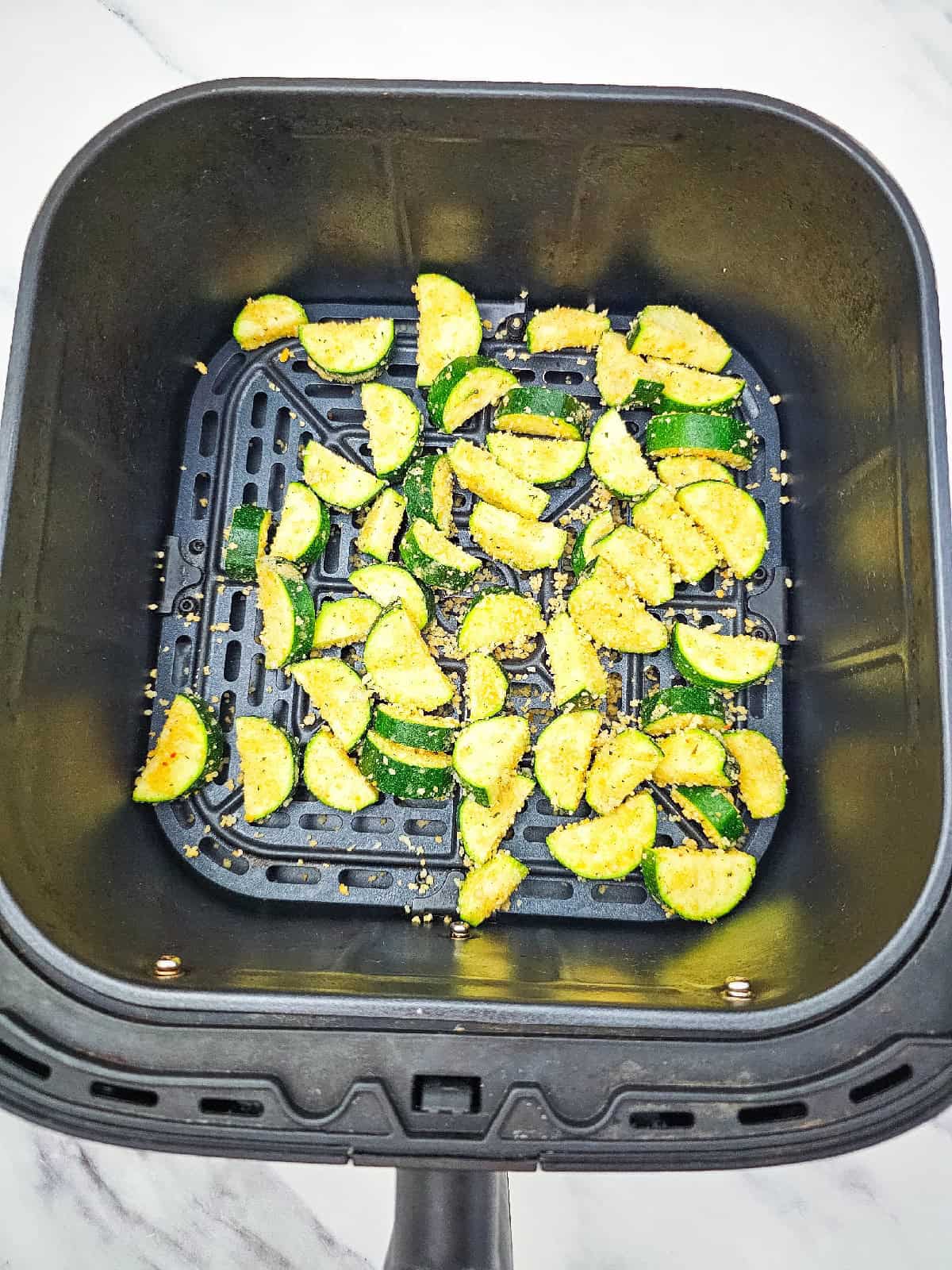 Breaded zucchini pieces arranged in a single layer inside an air fryer basket before cooking.