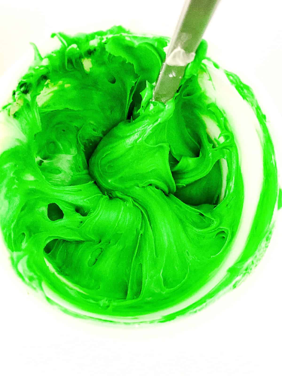 Bright green frosting swirled in a bowl after mixing with green food coloring for Christmas tree cupcakes.