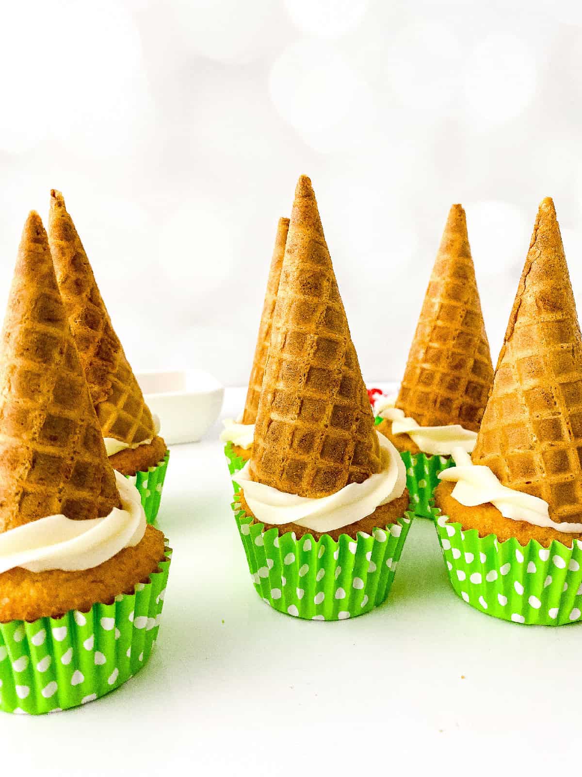 Side view of cupcakes with inverted waffle cones set on top of white frosting, creating the shape of a Christmas tree base.