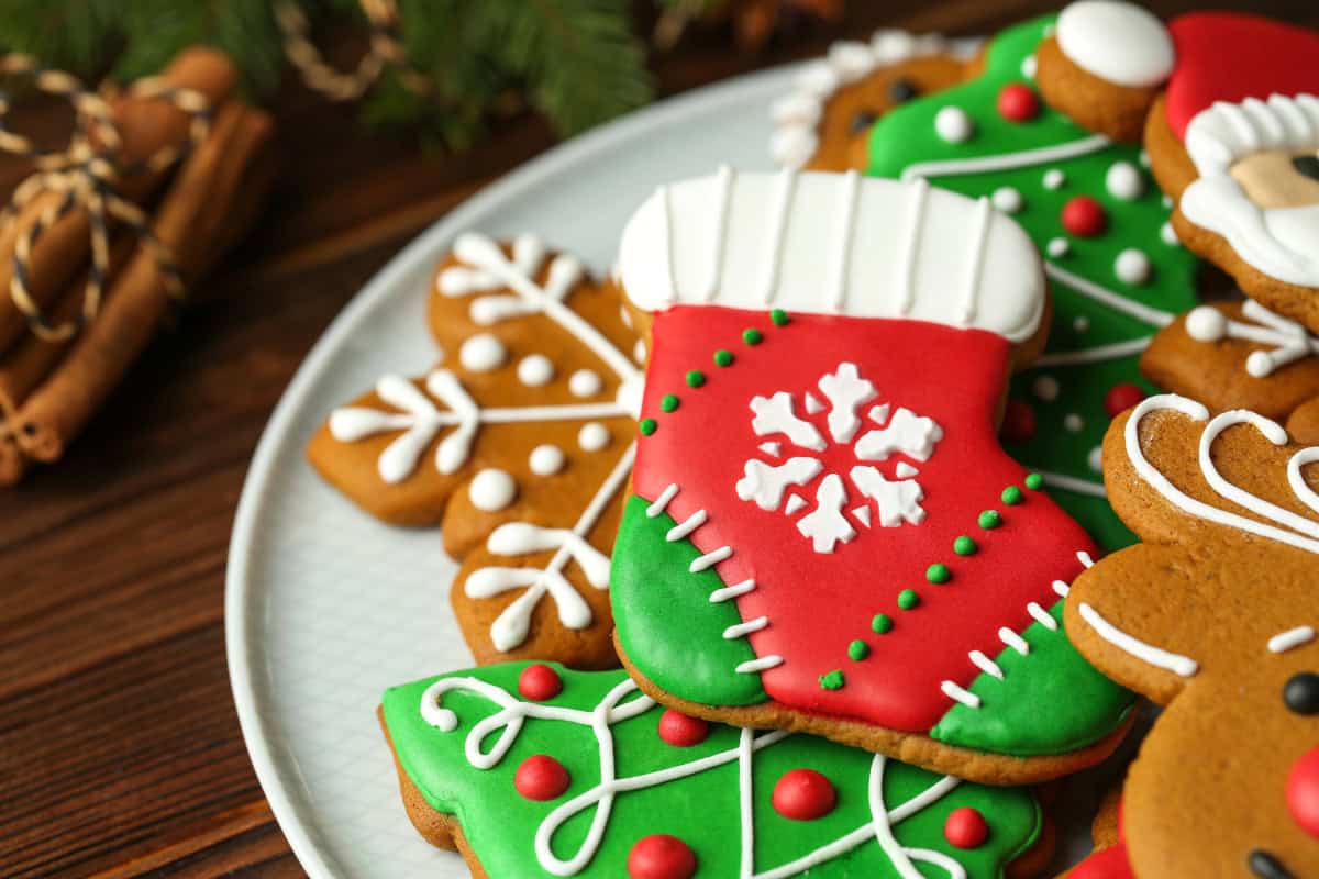 Christmas stocking-shaped cookie with red and green icing, surrounded by snowflake and tree cookies on a white plate for a cozy holiday dessert display.