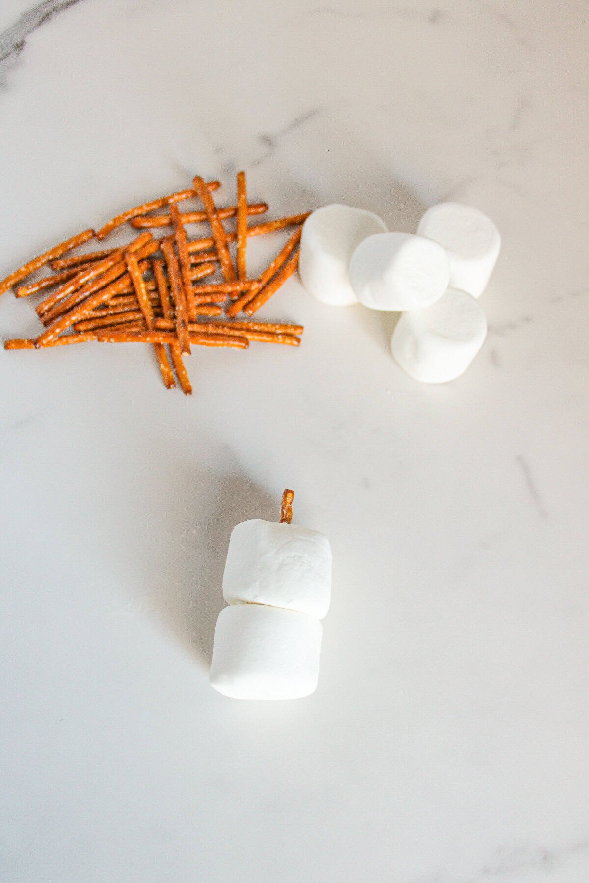 Two marshmallows stacked together with a pretzel stick inserted vertically through the center.