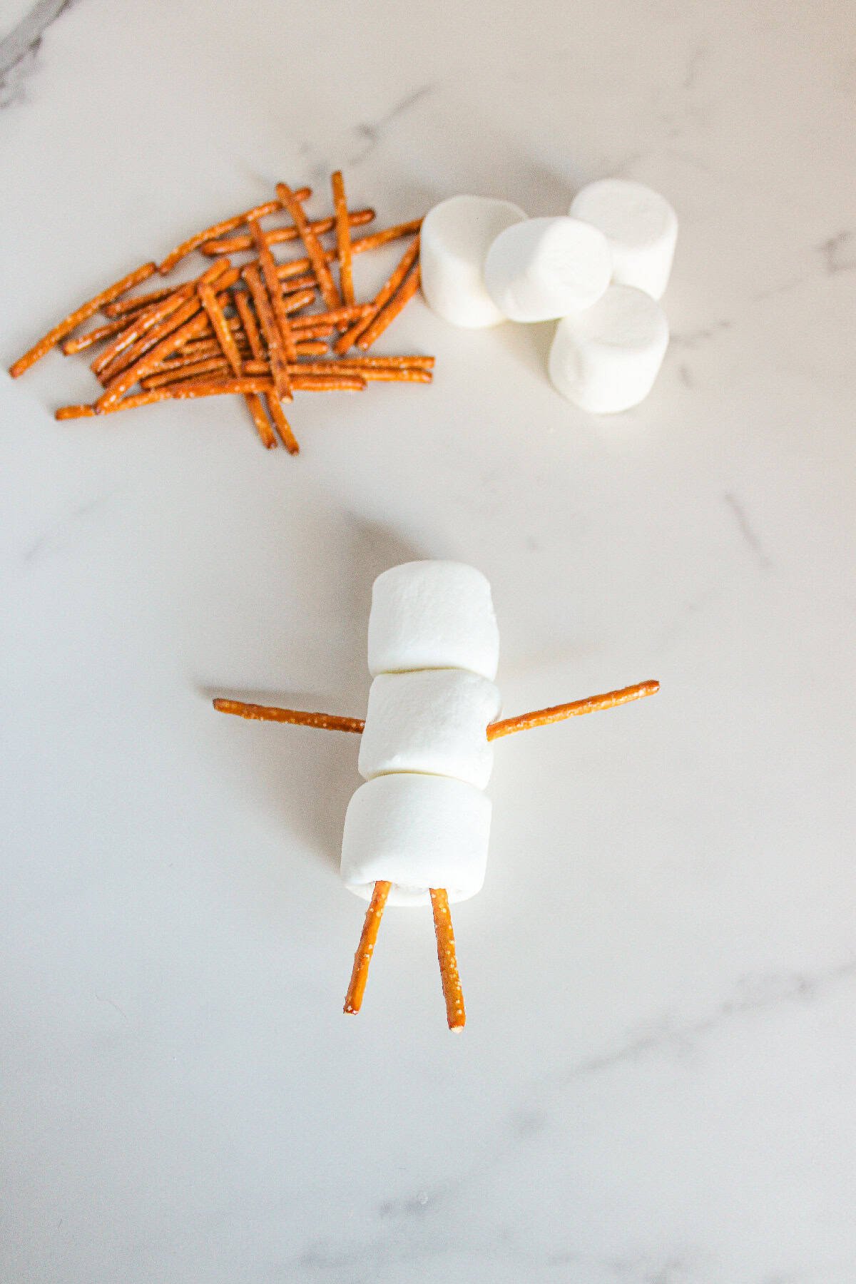 Pretzel sticks added as arms and legs to the marshmallow snowman body.