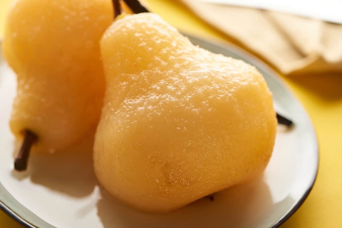 Soft, glistening poached pears served on a white plate against a warm yellow background, highlighting their tender texture and golden color.