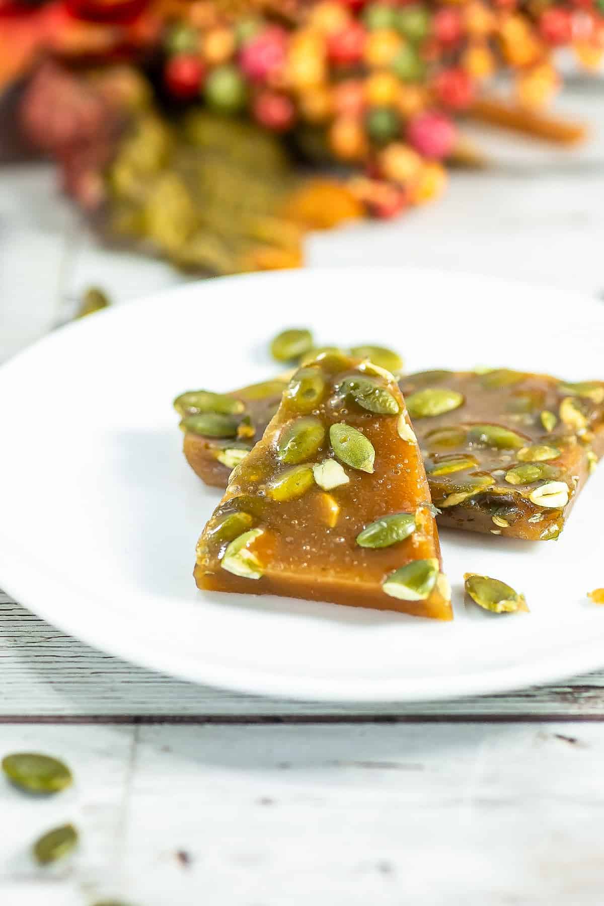 Pumpkin seed brittle triangle pieces on a white plate with autumn decor in the background.