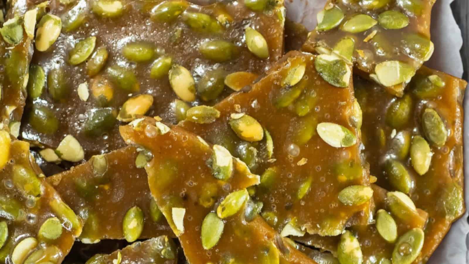Pumpkin seed brittle pieces stacked on parchment paper, showing caramel coating and green pumpkin seeds.