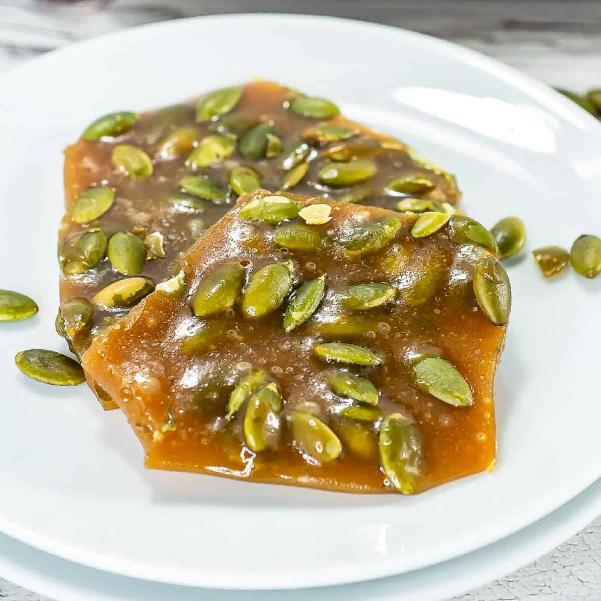 Pumpkin seed brittle triangle pieces on a white plate with autumn decor in the background.