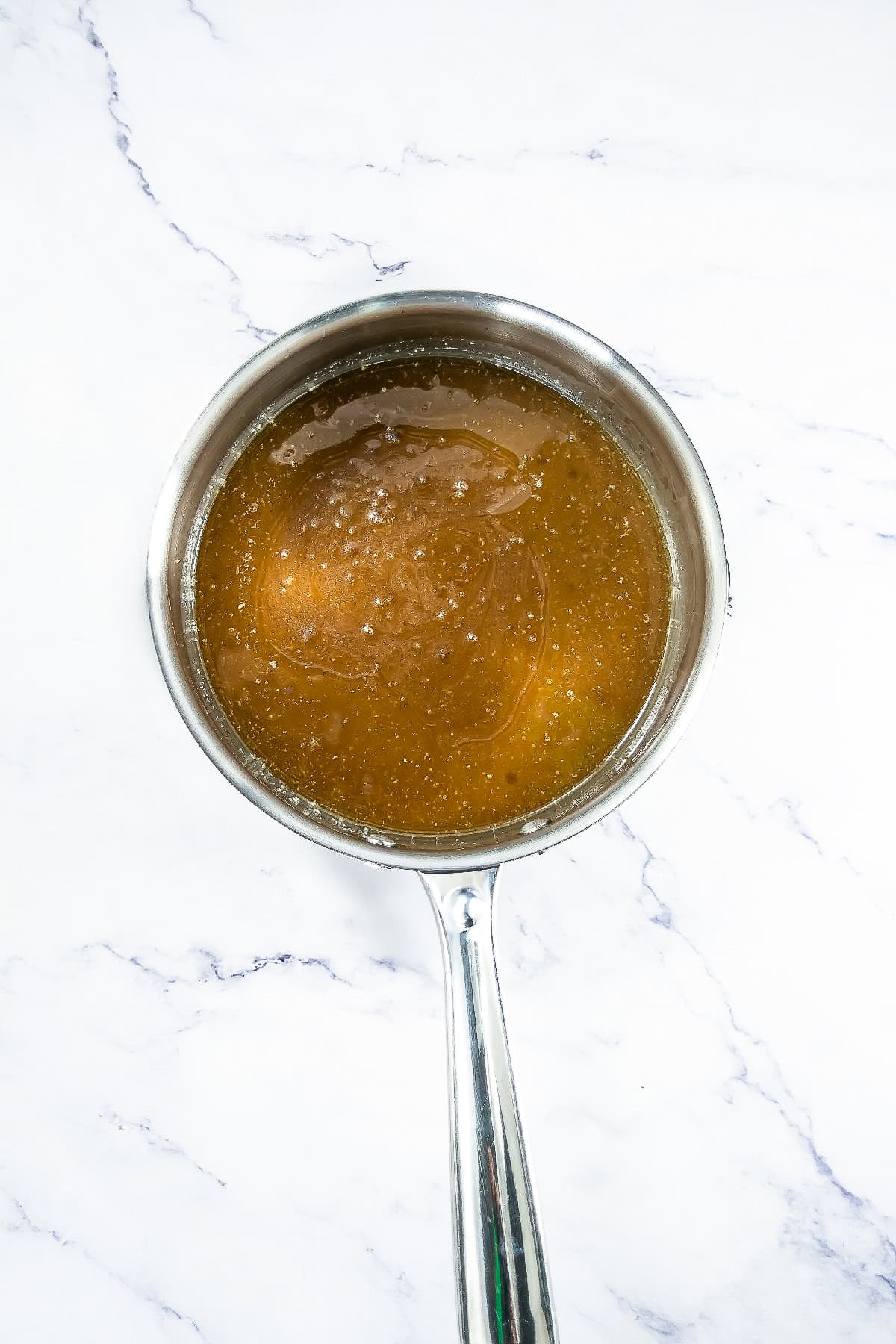 Melted butter, sugar, and honey mixture in a saucepan forming a smooth syrup.