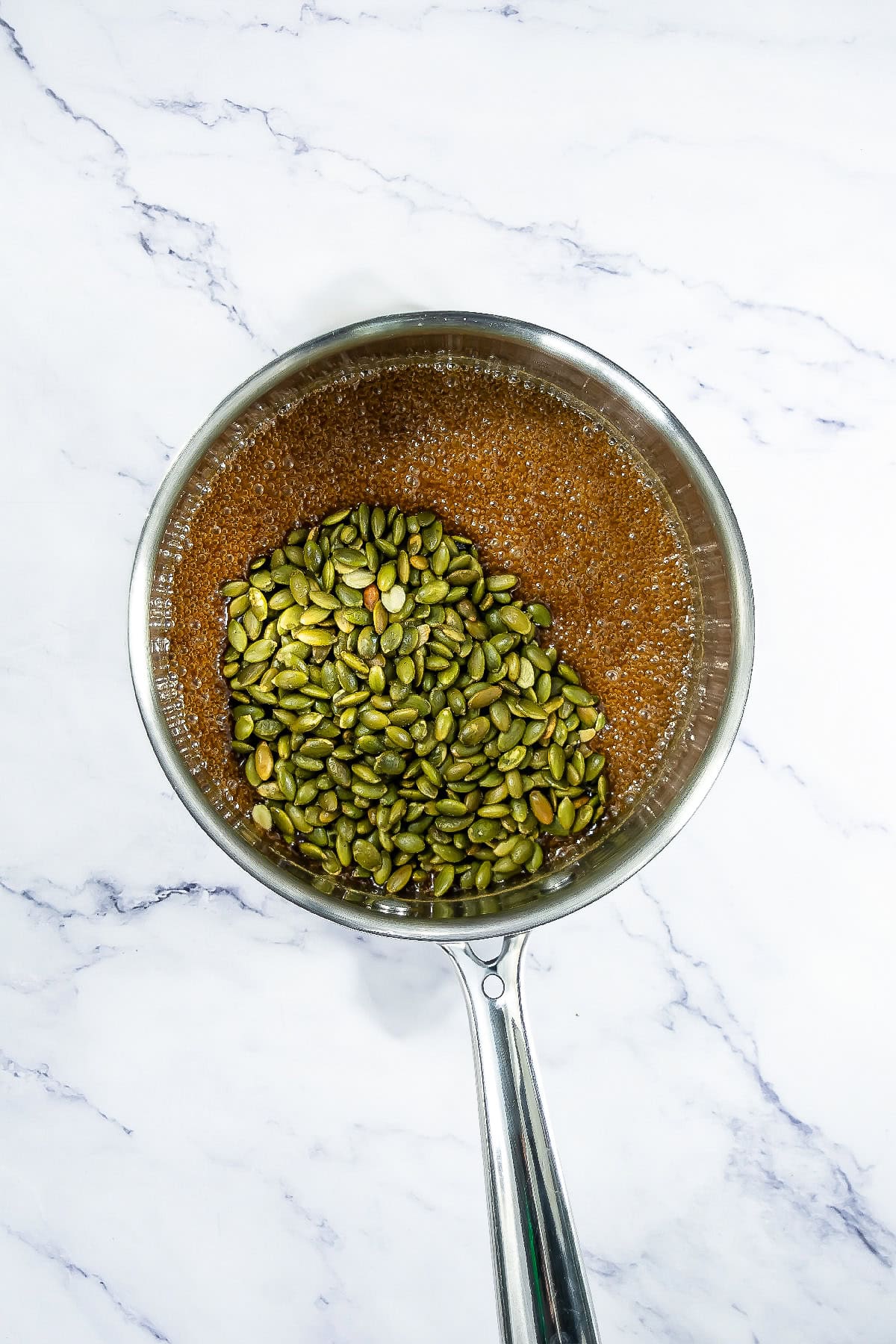 Pepitas poured into hot caramelized syrup in a saucepan.