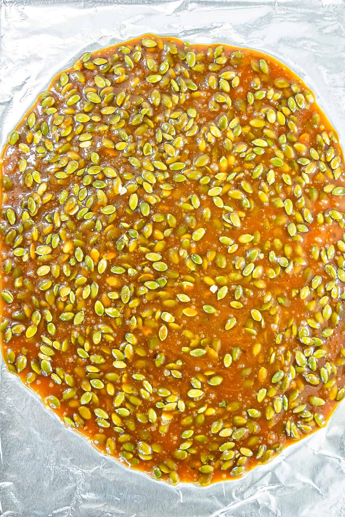 Hot pumpkin seed brittle mixture spread evenly on a foil-lined baking sheet.