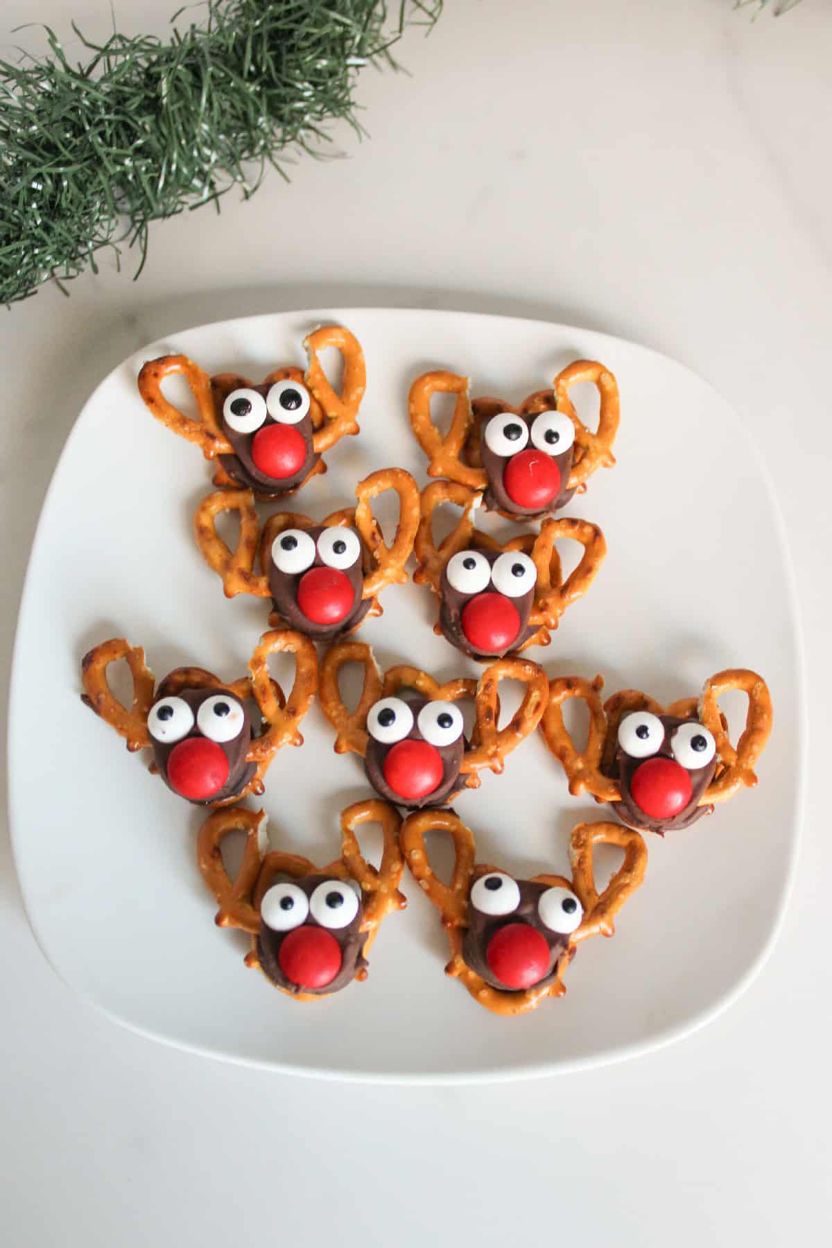 A plate filled with adorable Rolo pretzel reindeer treats, each with pretzel antlers, candy eyes, and a bright red nose, arranged in neat rows for serving.