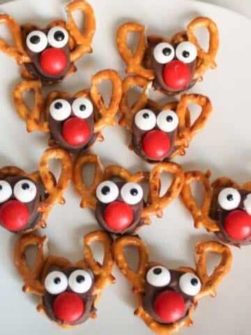 Festive reindeer treats made with mini pretzels, Rolo candies, red M&M noses, and candy eyeballs arranged on a white plate.
