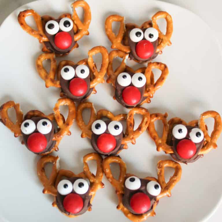 Festive reindeer treats made with mini pretzels, Rolo candies, red M&M noses, and candy eyeballs arranged on a white plate.