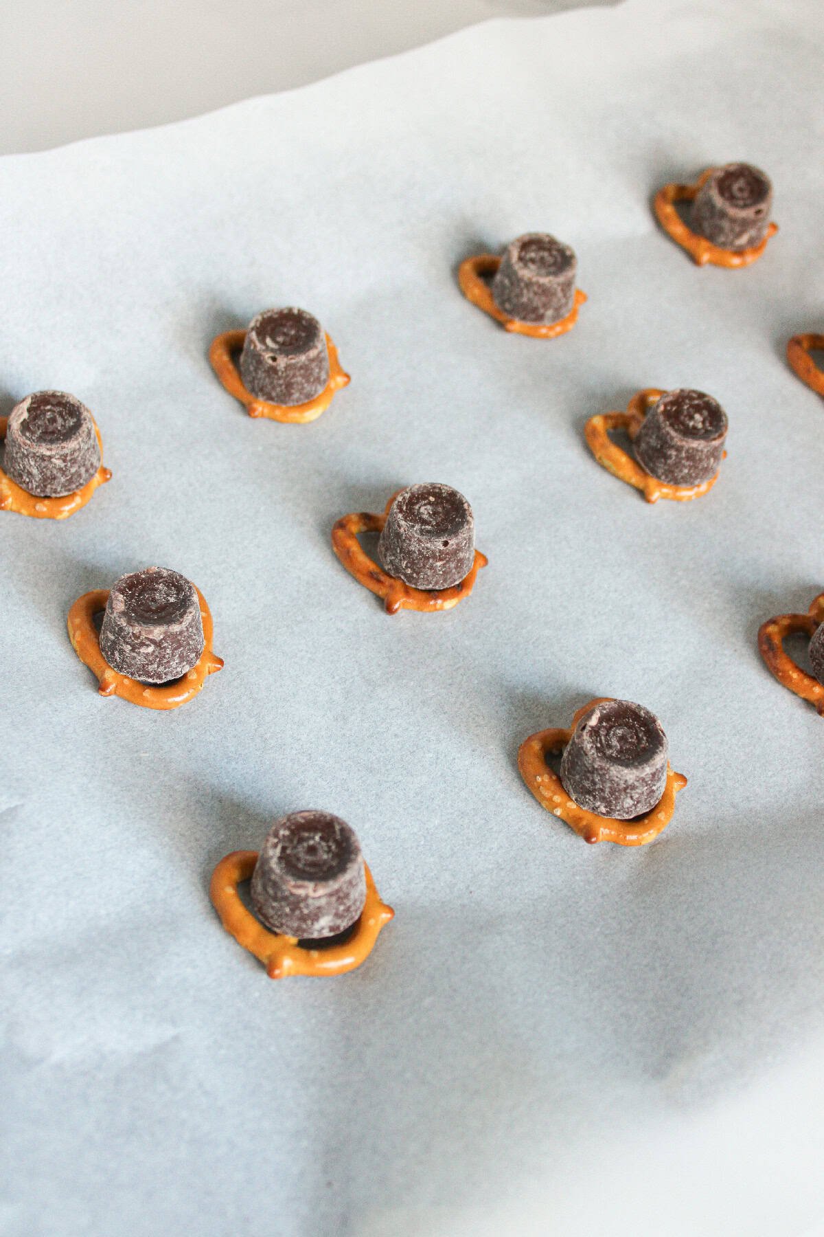 Chocolate Rolo candies placed on top of mini pretzels, evenly spaced on a parchment-lined baking sheet.