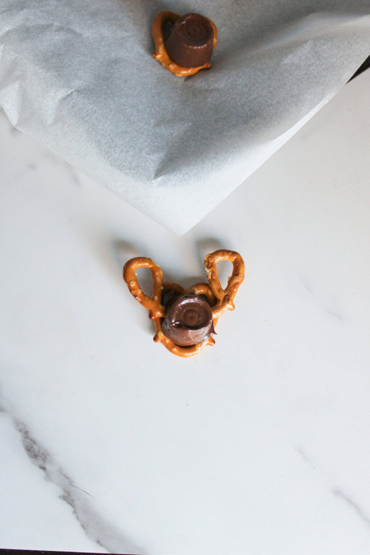 A Rolo candy on a pretzel base with two broken pretzel loops attached at the top to resemble reindeer antlers.