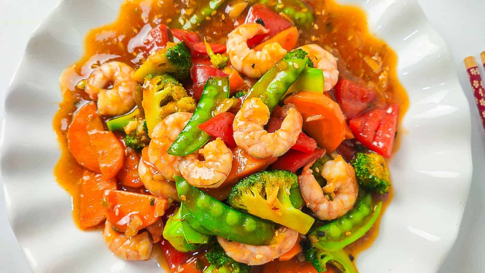 Overhead shot of shrimp and vegetable stir fry on a white scalloped plate.