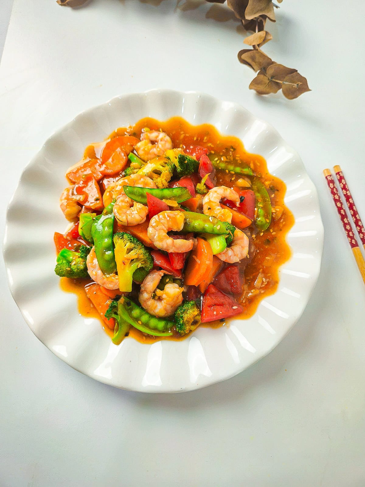 Overhead shot of shrimp and vegetable stir fry on a white scalloped plate, styled with chopsticks on the side.