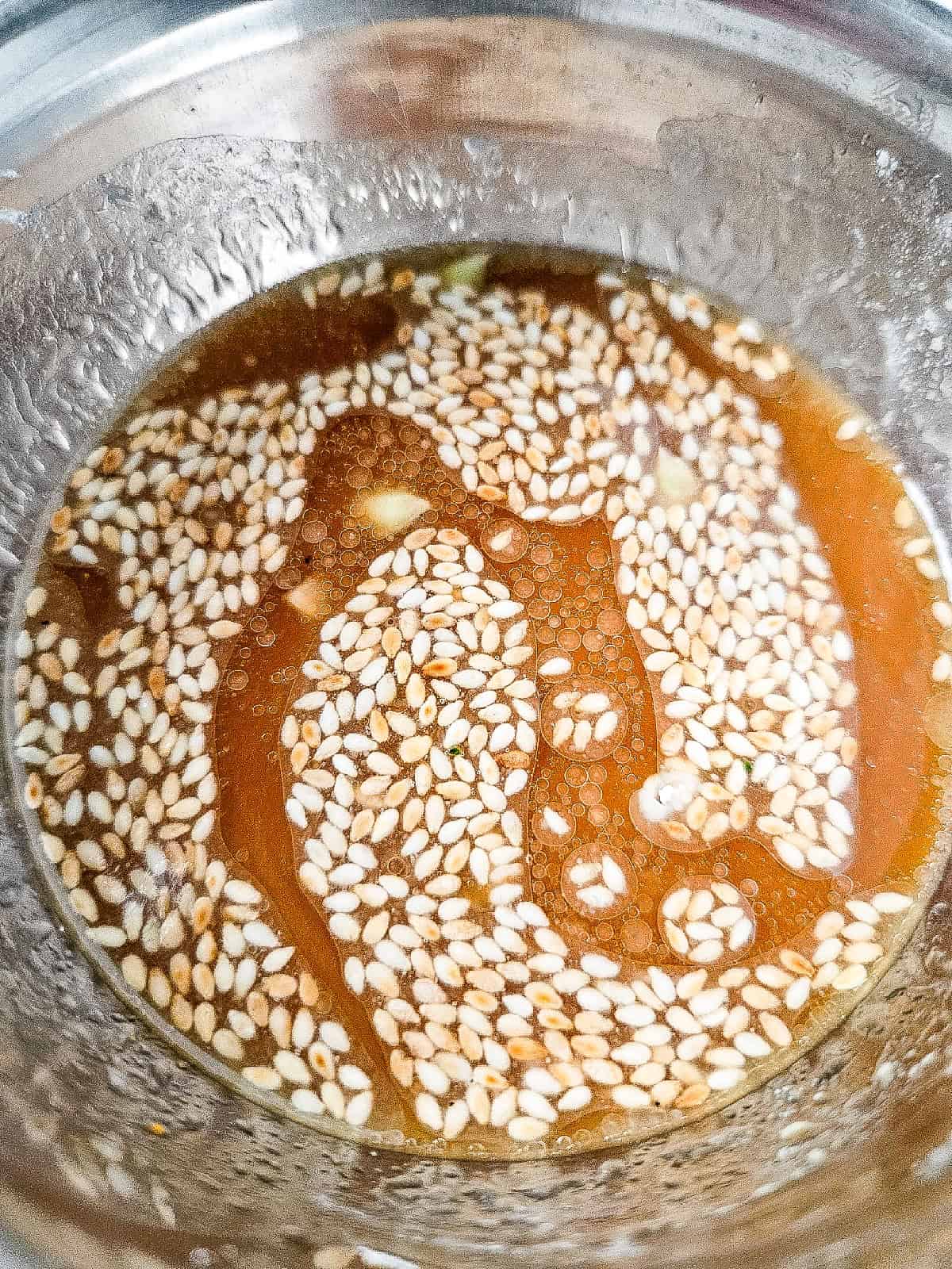 Sauce mixture with sesame seeds in a metal bowl for shrimp and vegetable stir fry.