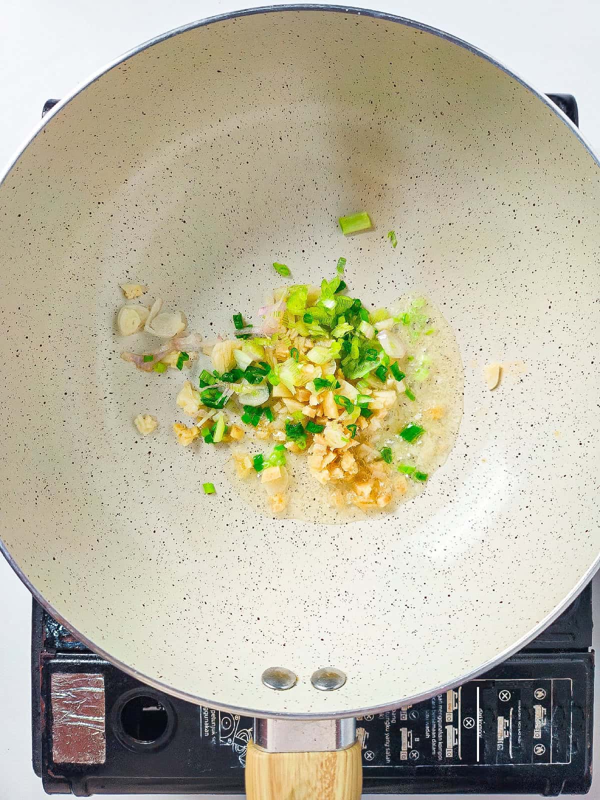 Cooking garlic, ginger, and green onions in a wok with oil for stir fry base.