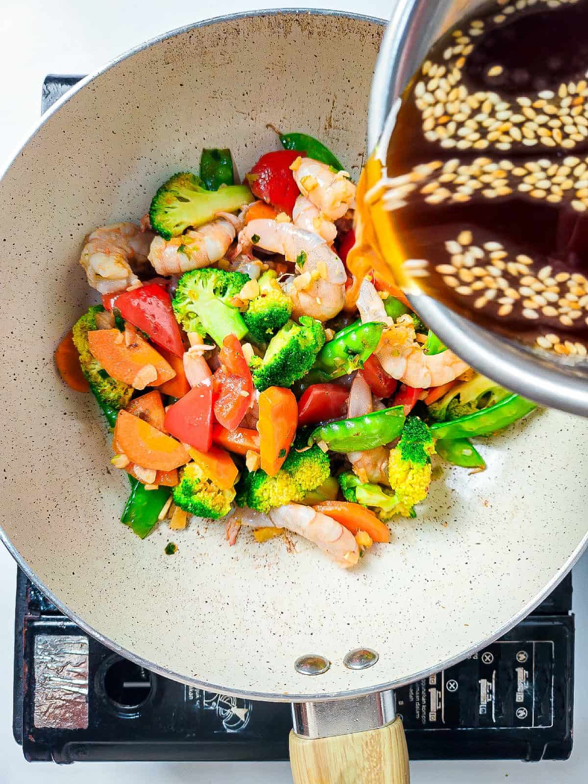 Pouring sesame soy stir fry sauce over shrimp and vegetables in a wok.