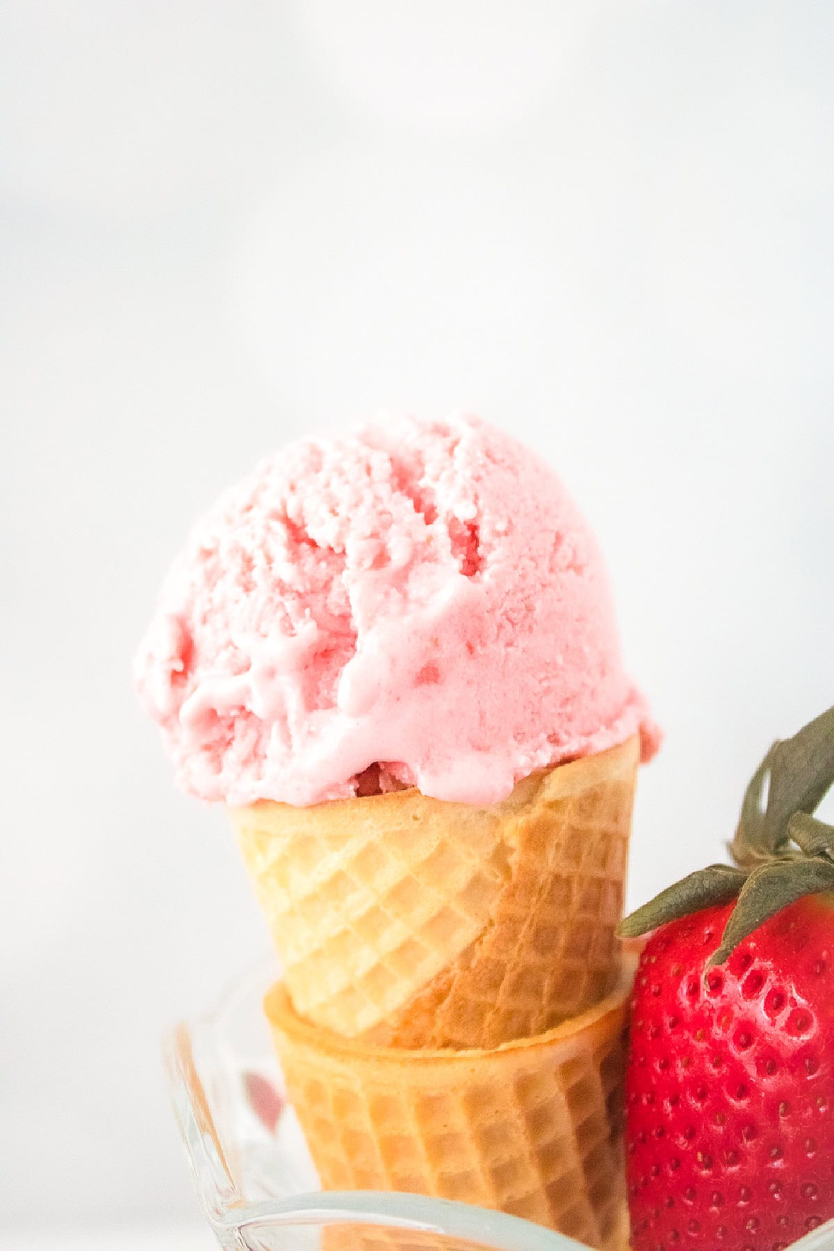 Close-up of a vegan strawberry ice cream cone with smooth pink texture and fresh strawberry beside it.
