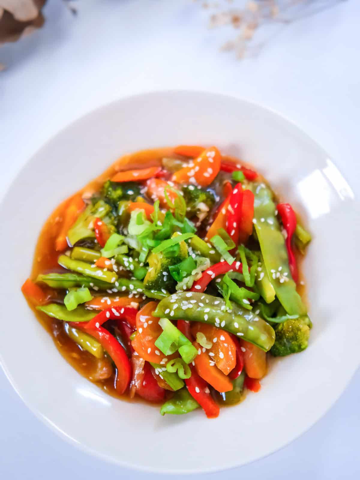 Teriyaki stir fry vegetables in a white bowl, topped with sesame seeds and fresh scallions for garnish.