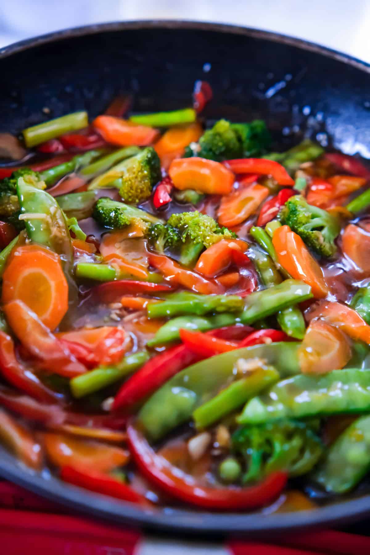 Close-up of veggie teriyaki stir fry with carrots, broccoli, bell peppers, and snow peas coated in thick glossy sauce.