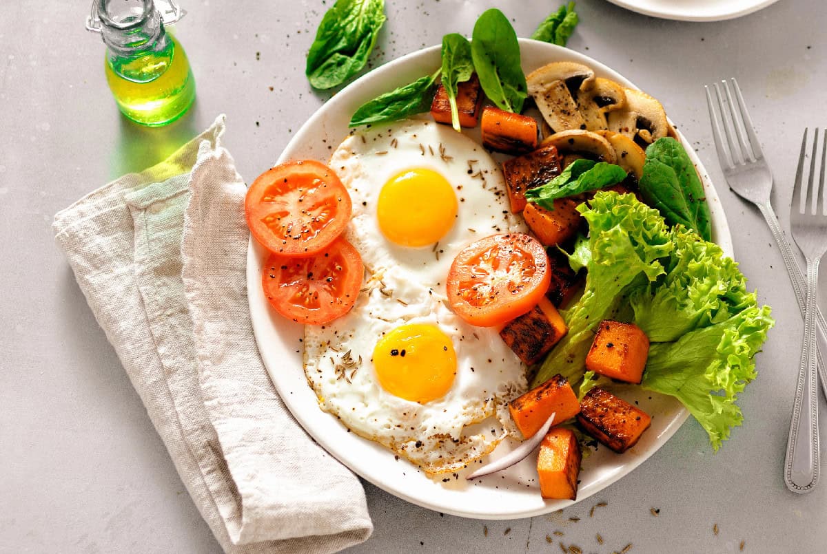 A balanced breakfast plate with sunny-side-up eggs, roasted vegetables, tomatoes, mushrooms, and fresh greens.