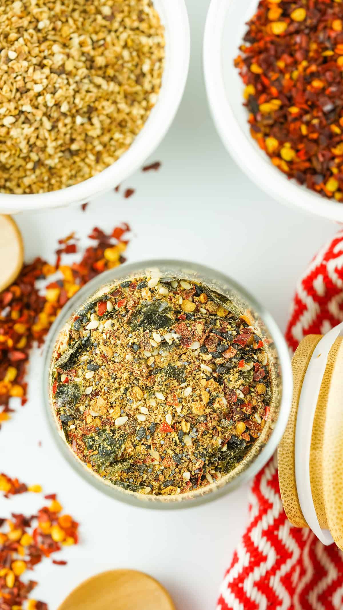 Top-down view of a glass jar filled with Japanese 7 spice blend, surrounded by chili flakes and toasted sesame seeds.