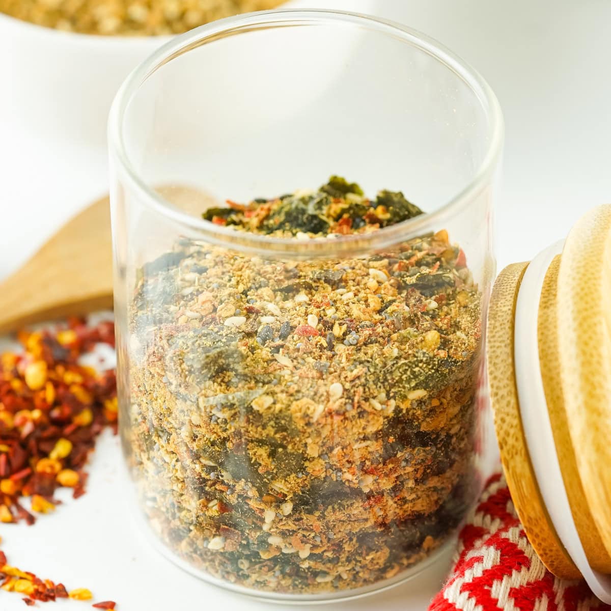 Close-up jar filled with homemade Japanese 7 spice blend, showing sesame seeds, seaweed, red pepper flakes, and aromatic seasonings on a bright kitchen surface.