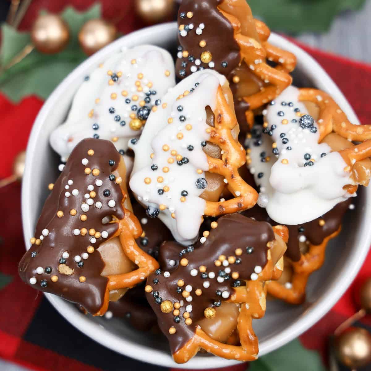 Bowl of New Year’s Eve dipped caramel pretzels shaped like holiday trees, covered in white and dark chocolate with festive gold and silver sprinkles.